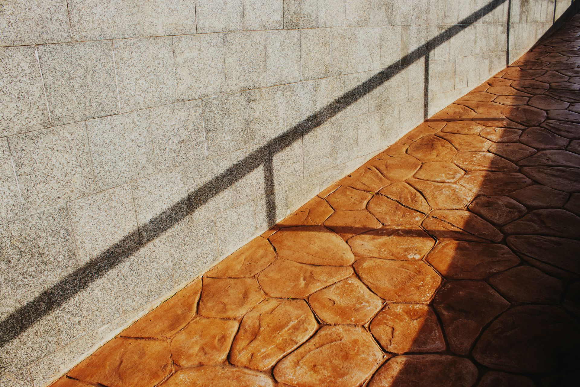 Shadows cast on a textured wall and patterned walkway